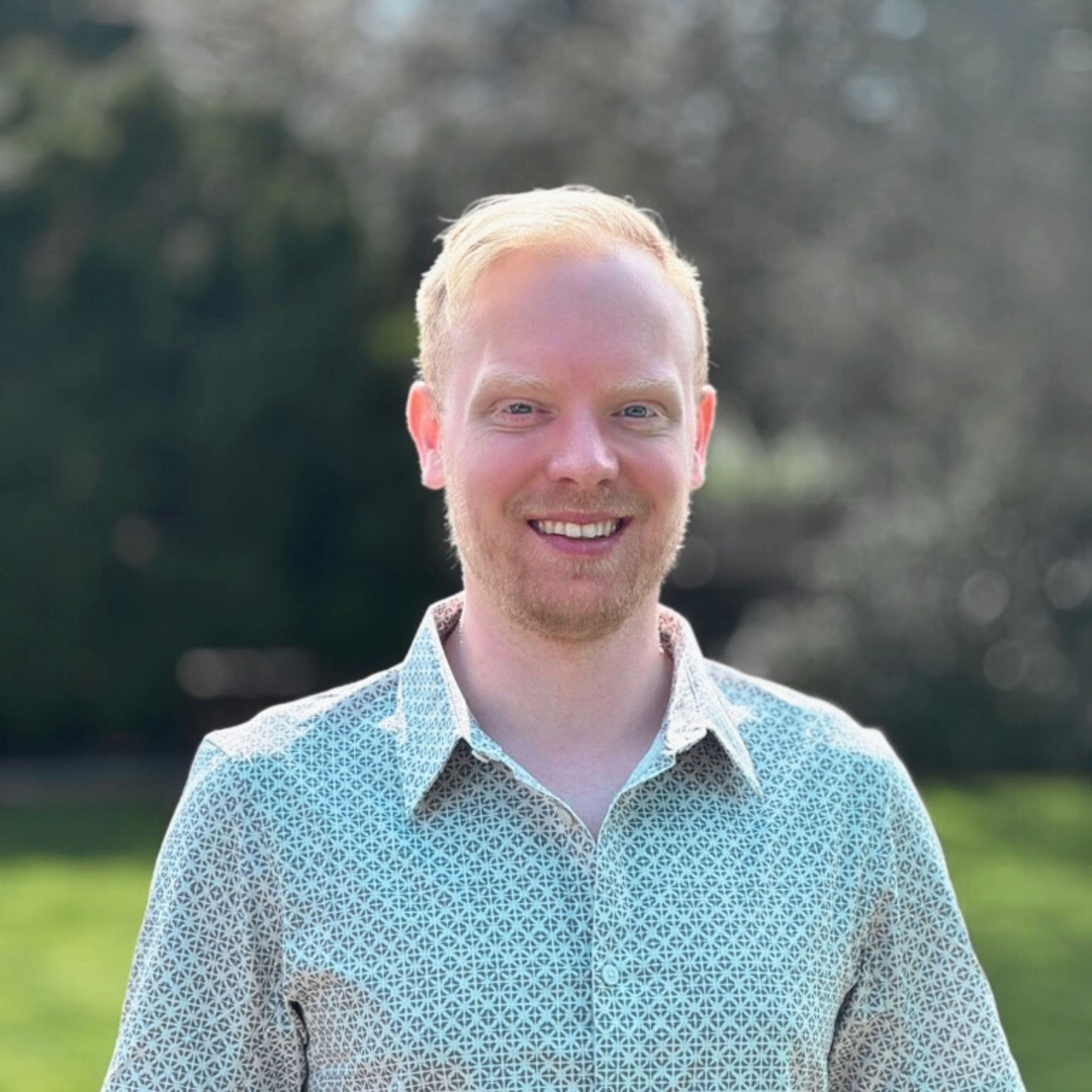 Smiling man in a patterned shirt outdoors.