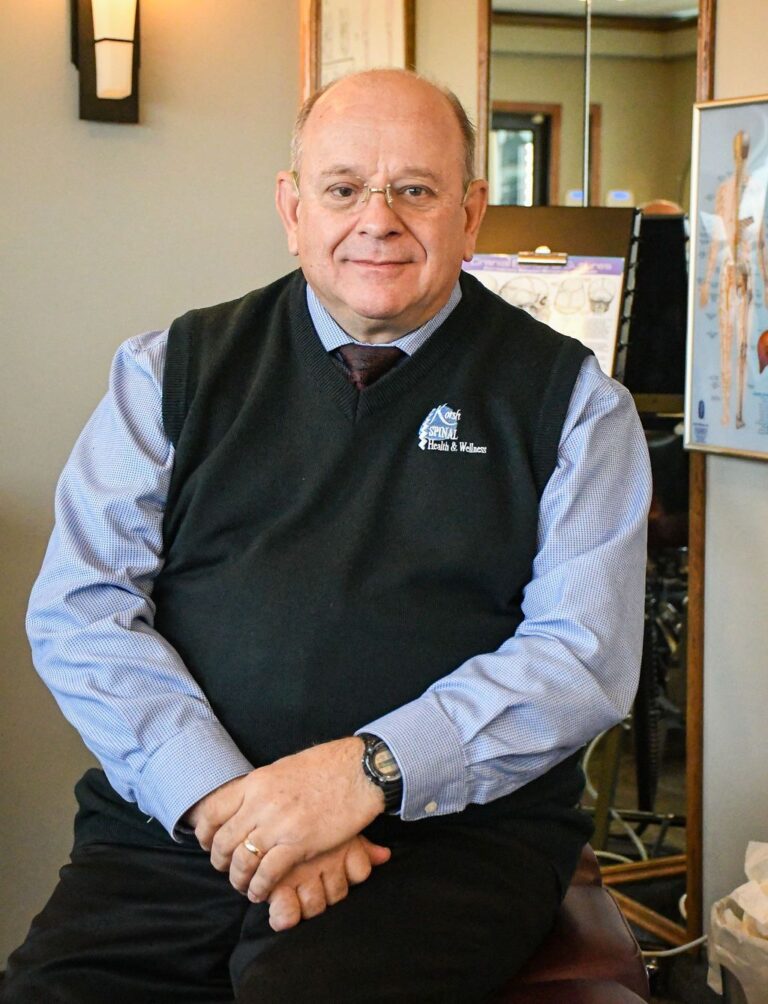 Individual sitting indoors, wearing glasses and a sweater.